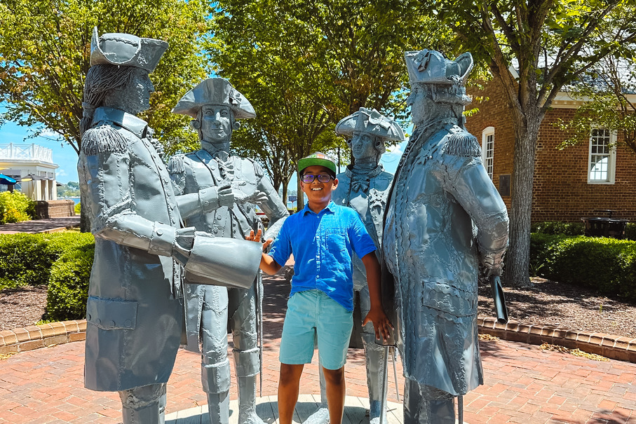 Visitors strolling along Riverwalk Landing and relaxing on Yorktown Beach with views of the York River and 18th-century architecture.